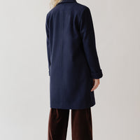 Back view of a woman standing wearing a navy blue wool coat and brown velvet pants.