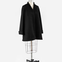 A sleek, vintage-inspired black wool swing coat displayed on a dress form for a woman. The black swing coat features a flared silhouette, long cuffed sleeves, and minimalist, elegant detailing, showcasing its classic design against a simple backdrop.