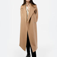 A fashionable woman showcases a straight-cut, full-length women's dress coat in a warm camel color, made from 100% wool. The coat features an oversized notched lapel that adds a contemporary touch to its classic design. Paired with sleek black trousers and a crisp white shirt, the ensemble exudes sophistication and elegance. The coat’s flowing silhouette enhances her confident stance, making it a perfect statement piece for any occasion.