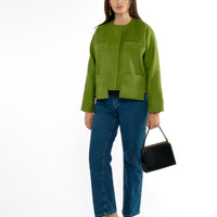 Full length view of a woman wearing jeans and a green lady jacket, holding a black purse, wearing black kitten heels.