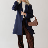 Woman laughing wearing a Navy blue wool coat, white blouse, brown velvet pants, and fun green eyeglasses
