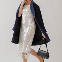 Woman wearing a sparkly dress with a navy blue wool coat.